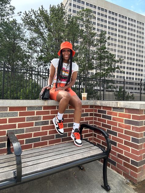 Girl sitting on a brick wall wearing a white, orange, pink, and black graphic tee, a orange bucket hat, black purse, orange biker shorts, white crew Nike socks, and Jordan 1 electro orange sneakers. Biker Shorts And Sneakers Outfit, Summer Jordan Outfits, Shorts And Socks Outfit, Outfit Biker Shorts, Sneaker Fits, Outfit Biker, Graphic Tee Outfit, Sneakers Outfit Summer, Car Letter