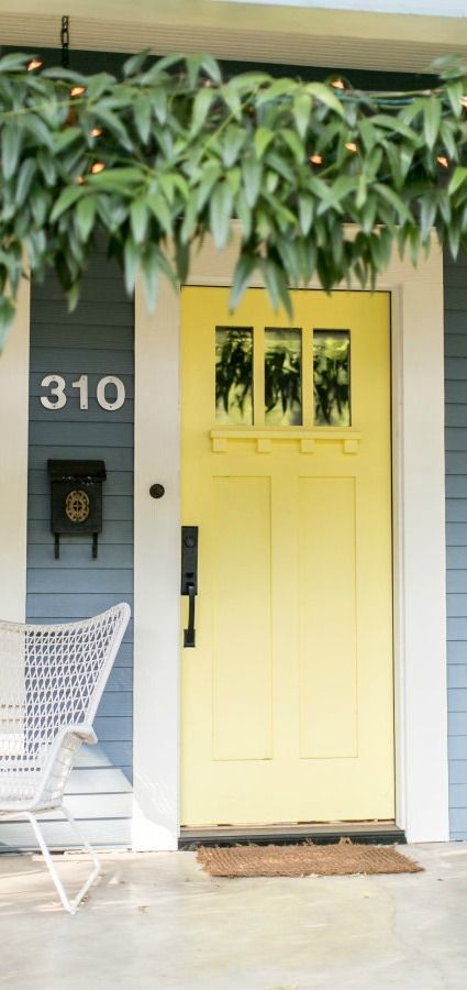 This bright yellow front door uses a coat of Upbeat from BEHR to add color and style to the exterior of this home. A bright white trim and darker blue gray siding complement the vivid color of this front door. Check out the rest of this post from the team at Style Me Pretty to find plenty of front door inspiration. Soft Yellow Front Door, Grey House With Yellow Door, House With Yellow Front Door, Pale Yellow Door, Pale Yellow Front Door, Yellow Exterior Door, Coloured Front Door, Gray Front Door Colors, Yellow Front Door