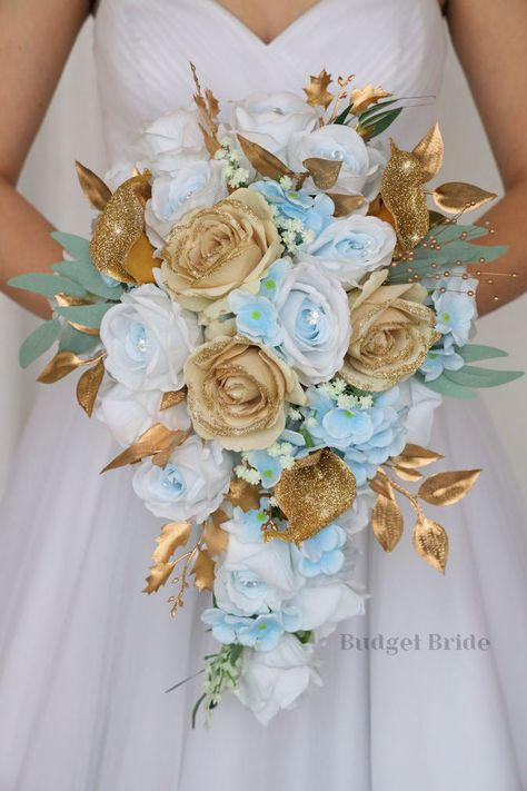 This lovely assortment of light blue roses with jewel centers and gold glitter tipped roses is bound to turn heads on your wedding day. This lovely cascading brides’ bouquet from the is an absolutely breathtaking arrangement for any bride to be, in any season. Sage greenery and gold glitter calla lily accents complete the look and add a delicate realism to this beautiful bouquet. This bouquet is 10” wide, 18” long, and is crafted by our in-house florists without using a foam base to anchor the f Cyan And Gold Wedding Theme, Blue And Gold Flower Arrangements, Blue And Gold Wedding Flowers, Sky Blue And Gold Wedding, Light Blue And Gold Wedding Theme, Tiffany Blue And Gold Wedding, Gold And Light Blue Wedding, Light Blue Gold Wedding, Light Blue And Gold Wedding