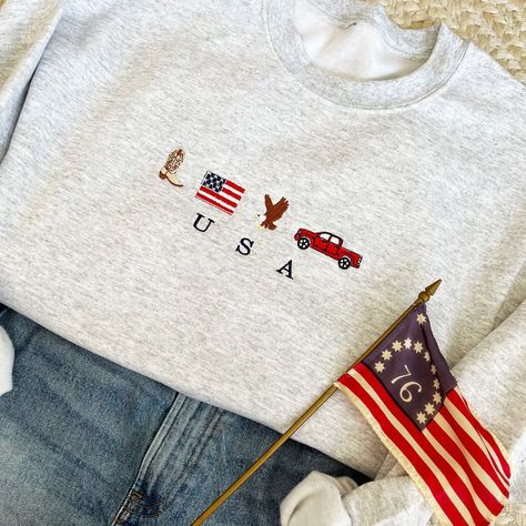 Celebrate the Red, White, and Blue in style with this USA embroidered American icons crewneck. Show off your patriotism with these icons designs and country western style! Rock your American pride! Super soft sweatshirt is Unisex fit, if you are looking for an oversized fit please size up! Design will always be embroidered as shown. USA will be embroidered in white on navy crews. Jada is wearing a size X-Large Ash for an oversized fit, she typically is a size small.  All sales are final due to customization of product. Will ship USPS or UPS unless requested otherwise. Colors may differ slightly from appearance on screen. Find us on Facebook at www.Facebook.com/ardenandgold , @ArdenAndGold , www.ardenandgold.com Usa Embroidery Designs, Sweatshirt Embroidery Ideas, Covington Ky, Usa Sweatshirt, Style Rock, American Icons, Embroidered Clothes, American Pride, Country Western