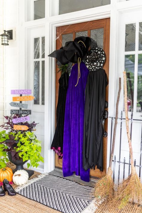 Brew up some Halloween magic by recreating this beguiling front porch vignette. Nestle twiggy broomsticks near your entry, then use command strips to hang three sweeping cloaks and pointy witch hats from the front door. Diy Halloween Wreaths For Front Door, Halloween Wreaths For Front Door Diy, Door Decorations Halloween, Halloween Entry Table, Halloween Wreaths For Front Door, Diy Halloween Door Decorations, Door Decor Ideas, Halloween Diy Outdoor, Halloween Front Porch Decor