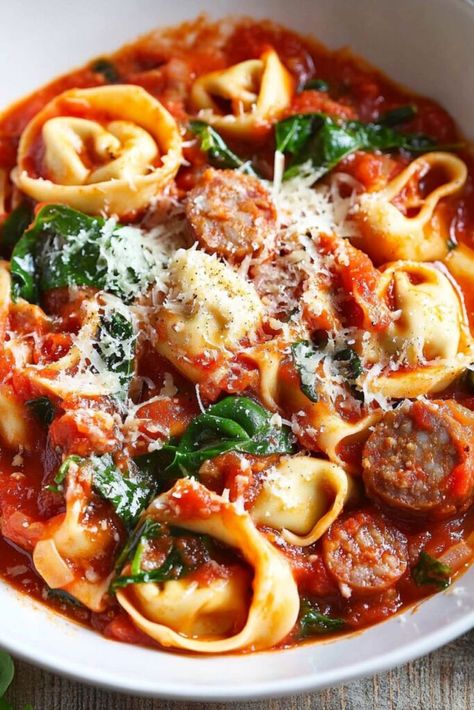 A close-up image of Tuscan tortellini pasta with Italian sausage, spinach, and a rich tomato-based sauce, served in a white bowl. The dish is topped with shredded Parmesan cheese and garnished with fresh herbs. The tortellini is tender, and the sausage bits are mixed into the sauce, creating a hearty and flavorful Italian meal, perfect for busy weeknights. Cooking For 3, Pasta Casseroles Baked, Oven Pasta Recipes, Italian Sausage Pasta Recipes, Italian Recipes For Dinner, Baked Casseroles, Pasta Recipes Quick, Italian Sausage Recipes Pasta, Creamy Pasta Bake