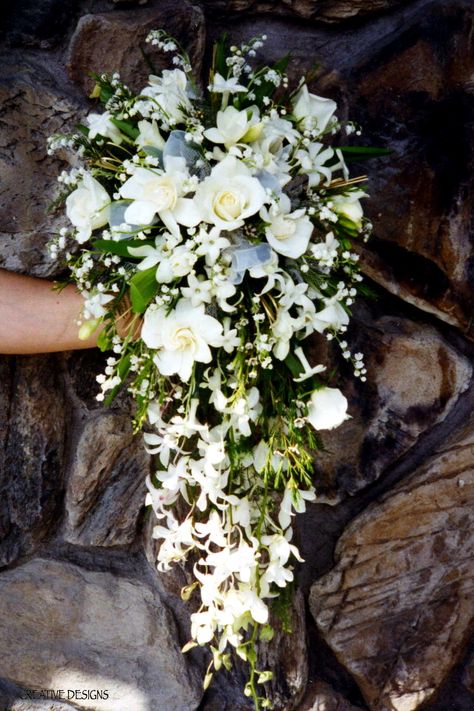 Lily of the Valley dominate this Open End Cascade Bouquet of White Roses, Gardenias, Dendrobium Orchids, Stephanotis, Freesia, White Wax Flower with White Sheer Ribbon accent in Center. White Gardenia Bouquet, Waterfall Bouquet Wedding, Gl Wedding, Orchid Waterfall Bouquet, Wedding Bouquets Roses, All White Cascading Bouquet, Lily Of The Valley Bridal Bouquet, Cascading Bouquet White, Waterfall Bouquet