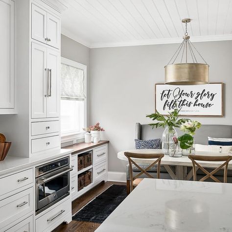 A window dressed in a gray and white roman shade is framed by light gray wall paint and positioned above white shaker cabinets fitted with a wood countertop and fixed flanking shelves holding woven baskets. Small American Kitchens, Built In Buffet, Dark Brown Cabinets, Gray Painted Walls, Kitchen Goals, Transitional Dining Room, White Shaker Cabinets, Brown Cabinets, Light Grey Walls