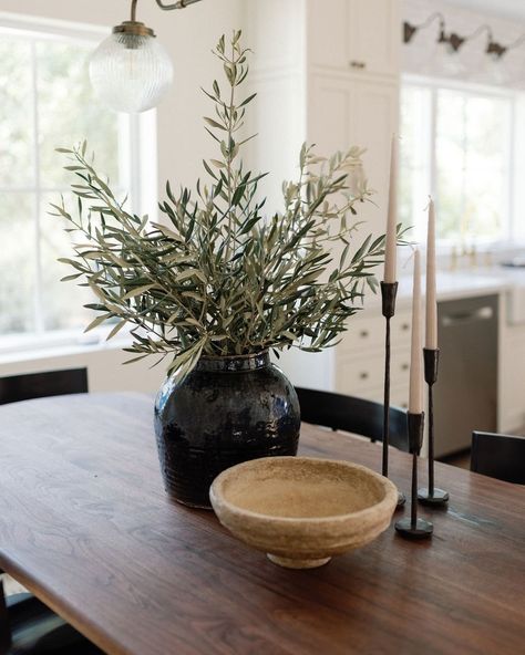 Image Details: black glazed textured vase with olive stems, wood bowl, and black iron taper candle holders on a dark brown wood table. Dining Table Black Vase, Dark Academia Dining Table Decor, Candle Holders Dining Table, Greenery On Black Tablecloth, Centerpieces Everyday Table, Staged Dining Table, Black Dining Room Table Centerpiece Ideas, Dark Wood Table Setting, Wood Table Centerpieces Dining Rooms