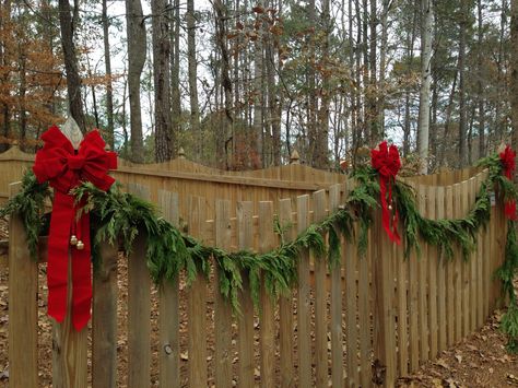 Christmas fence, greenery garland red bow jingle bells! Christmas Outdoor Fence Decorations, Wood Fence Christmas Decorations, Christmas Fence Decorations Outdoor Red Bows, Fence Garland Christmas, Garland On Fence, Garland On Fence Christmas, Christmas Garland Fence, Fence Christmas Decorations, Holiday Fence Decorating Ideas