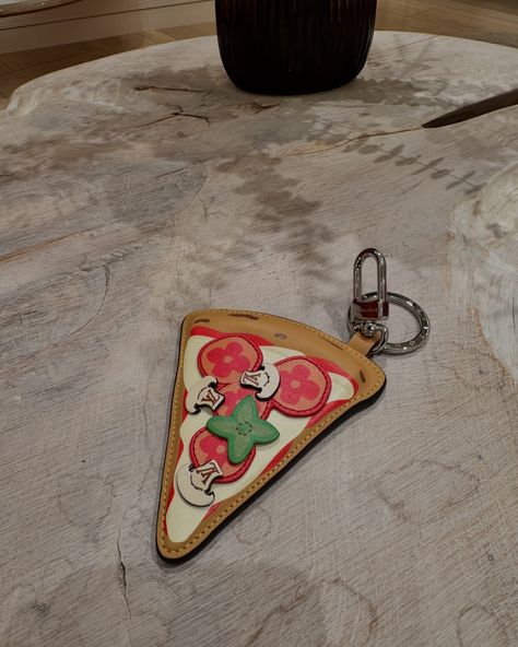 The LV Burger Bag Charm playfully reinterprets a classic House symbol, adding it to the diner sandwich—green lettuce, red tomato, yellow cheese, and Monogram bread included. With a silver-toned zip closure, the leather pouch hooks onto belt loops for instant joy and can hold a wireless earphones case. A unique gift, the multicolored LV Pizza Key Holder and Bag Charm is pure fun. The House heritage is translated into leather toppings: red pepperoni and green basil with Monogram Flowers, and ... House Symbol, Green Lettuce, Red Tomato, Bag Charms, Earphone Case, Car Keychain, Wireless Earphones, Classic House, Leather Pouch