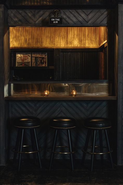 The interior features brass details, dark wood chevron walls, and tufted leather seating. Dark Bar Interior, Dark Wood Bar, Chevron Walls, Dark Bar, Lighting Aesthetic, Books Kitchen, Bar Ceiling, Gold Diggers, Wood Bar Table