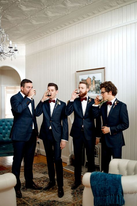 Grooms in their black suits and burgundy bow ties relaxing and sharing a drink before the wedding ceremony at Gabbinbar Homestead. Navy Suit Burgundy Tie Wedding, Groom Winter Wedding Attire, Navy Blue Groomsmen Suits Burgundy, Groom And Groomsmen Attire Burgundy, Black And Burgundy Groomsmen Attire, Navy Burgundy Groomsmen, Winter Groomsmen Attire Burgundy, Navy Suit Burgundy Bow Tie, Groomsmen Colors