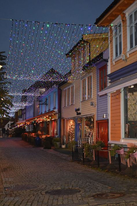 Twinkle lights shimmer over a cobblestone walkway lined with colorfully painted buildings. Norway City, Norway House, Stavanger Norway, Norway Travel, Colourful Buildings, Stavanger, Dream Holiday, White Houses, Scandinavia