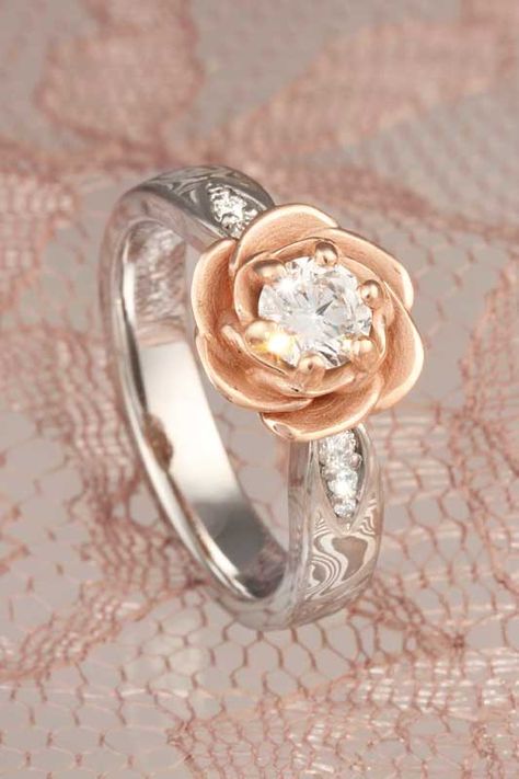 A blossoming rose cradles the center diamond or sapphire in this floral engagement ring. The rose is planted on a band of mokume gane, with 0.09 ctw diamond accents in leave-shaped recesses. This design is a great choice for modest-sized center stones, but can also be scaled up for larger stones. Rose Shaped Engagement Ring, Flower Setting, Gothic Engagement Ring, Engagement Ring Inspiration, Floral Engagement Ring, Mokume Gane, Flower Engagement Ring, Gold Diamond Wedding Band, Classic Engagement Rings