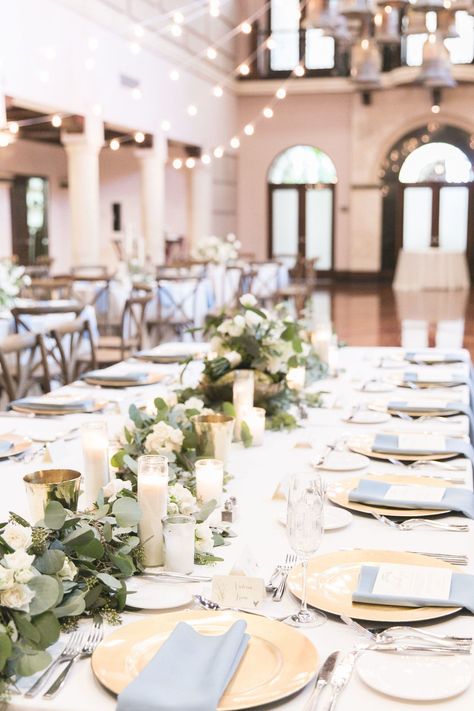 head table is dressed with white linens, french blue napkins, gold chargers, hand water colored menu cards, a lush garland of silver dollar eucalyptus and seeded eucalyptus and candles. Slate Blue Wedding, French Blue Wedding, Blue Table Settings, Blue Wedding Centerpieces, White Linens, Gold Chargers, Dollar Eucalyptus, Blue Napkins, Seeded Eucalyptus