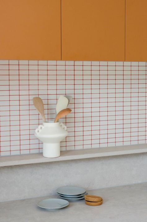 White tiles with orange grout in kitchen with orange cabinetry Orange Grout Kitchen, Colour Grout Kitchen, White Tile Orange Grout, Kitchen Tiles Aesthetic, White Kitchen Coloured Backsplash, White Tiles Coloured Grout Bathroom, Kitchen Orange Tiles, Coloured Grout Kitchen, Colored Grout White Tile