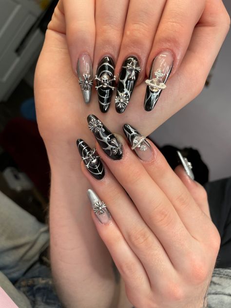 Long acrylic nails painted black with silver details and charms Acrylic Nails Rockstar Girlfriend, Heavy Metal Inspired Nails, Goth Rhinestone Nails, Emo Nails Y2k, Grunge Nails With Charms, Black Nail Designs Emo, Nail Rock Style, Goth Charm Nails, Black Nail Designs Y2k