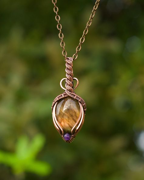 "This gemstone pendant features a flashy orange labradorite oval with a faceted royal purple amethyst accent. The crystal is wire wrapped in pure copper with a triple wire bail that is twisted into a Celtic braid design with minimal coverage on the front of the stone. The wire has been antiqued and hand polished for an antique look. This unisex pendant comes with an 18\" antique copper plated chain and lobster clasp. If you prefer a different length, let me know and I will gladly customize your chain for you. You can upgrade to a pure copper ball chain for $5. It ships for free in US in a gift box. If you are sending this as a gift to someone else, I will happily include a handwritten card with a message from you! Just let me know what you'd like to say." Diy Necklace Designs, Celtic Braid, Wire Wrap Cabochon, Wire Jewelry Rings, Wire Wrap Jewelry Designs, Instruções Origami, Wire Wrapped Jewelry Diy, Wire Wrapped Crystal, Bijoux Fil Aluminium