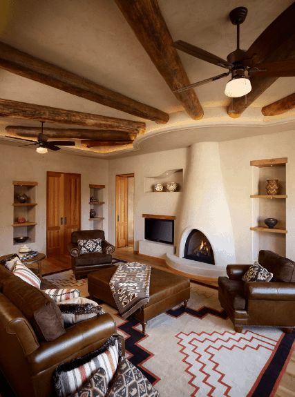 Cozy living room features a kiva fireplace accented with round wood beams. It faces the brown leather sofa set filled with patterned and striped pillows. Southwestern Living Room Ideas, Adobe Fireplace, Southwestern Homes, Southwestern Interior, Southwestern Living Room, Southwest Living, Rustic Family Room, Southwest Home Decor, Santa Fe Home