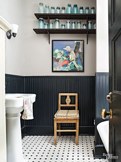 The molding top and bottom beadboard.......,,,,,,,,,,little bit country, a little bit cottage, this bathroom pays tribute to long-ago lavatories in modern ways. References to farm life include a rural rendering, a canning-jar collection, and a primitive coverlet folded on an antique chair. The tiled floors and black painted wainscoting give a nod to cottage style in high-impact fashion. Country Cottage Bathroom, Country Bathroom Designs, Black Wainscoting, Wainscoting Stairs, Painted Wainscoting, Cottage Bathroom Ideas, Wainscoting Bathroom, Cottage Bath, Primitive Bathrooms