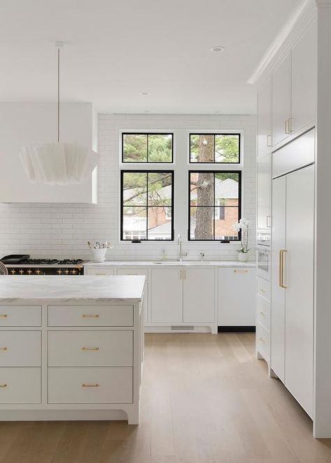 Stacked white flat front doors fitted with brass pulls accent a kitchen island topped with a white and gray marble countertop lit by modern white chandeliers. Flat Front Kitchen Cabinets, Flat Kitchen Cabinets, Flat Panel Kitchen Cabinets, Flat Front Cabinets, Island Drawers, Flat Cabinets, Kitchen Island Tops, Cottage Kitchen Design, Flat Panel Cabinets