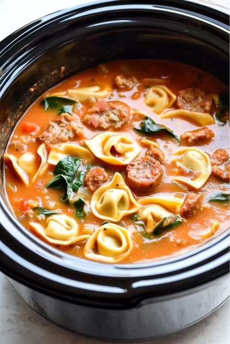 A hearty Italian slow cooker soup with cheese tortellini, sausage, carrots, spinach, and tomatoes in a crockpot, simmering in a creamy tomato broth. Crockpot Italian Sausage Tortellini Soup, Tortellini Slow Cooker Recipes, Slow Cooker Tomato Tortellini Soup, Tomato Tortellini Soup Crockpot, Soup With Cheese Tortellini, Crockpot Tortellini Soup, Tortellini Soup Crockpot, Crockpot Italian Sausage, Crockpot Tortellini