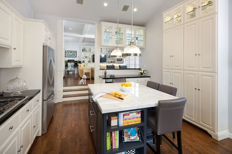 Gorgeous sunken kitchen boasts white cabinets adorned with brushed nickel hardware alongside sleek black perimeter counters which stand alongside a counter depth stainless steel two door refrigerator with freezer door across from wall filled with full height pantry cabinets. Sunken Kitchen, Interior Column Design, Light And Bright Kitchen, Light In The Kitchen, Split Level Kitchen, Kitchen Keeping Room, Kitchen Pass Through, Two Door Refrigerator, Contemporary White Kitchen