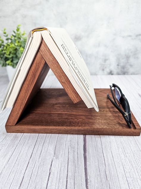 ✦ Free Shipping ✦ Can Be Personalized ✦ Handcrafted in Tennessee This solid walnut or maple book placeholder seamlessly blends beauty with practicality. The triangle point is used to hold your place in the book, and the base has a groove routed out to hold a pen or pencil, your glasses, tube of ChapStick, or anything else you want to keep close by. The side can have an optional engraving of a minimalist line drawing of an open book.  The whole piece is 11" long, 8" wide, and 7.5" tall. It comes Diy Nightstand Book Holder, Book Rest Diy, Triangle Book Holder, Book Place Holder, Book Stand Design, Reclaimed Wood Tray, Wood Pallet Recycling, Minimalist Line Drawing, Book Rest