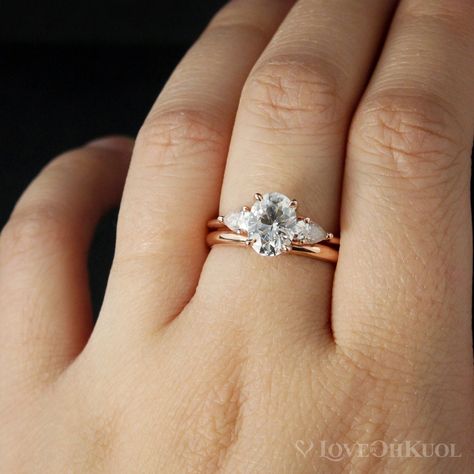 Here is a gorgeous 3 stone engagement ring with classic clean lines. The center stone features a stunning oval brilliant -cut Forever One Colorless D/E/F grade Moissanite, accented with two pear-cut Forever One Colorless moissanites on each side. The band is half round and is 1.5mm wide. The raised shoulders allows this ring to stack easily with all our wedding bands. This ring is also available with a round center stone too.  Paired together with our Comfort Fit Wedding Band. The wedding band h Three Stone Engagement Rings Oval, Wedding Ring Sets Simple, Rose Gold Wedding Ring Sets, Gold Band Wedding Ring, 14k Rose Gold Wedding Ring, Trilogy Engagement Ring, Simple Wedding Bands, Comfort Fit Wedding Band, Moissanite Engagement Ring Oval