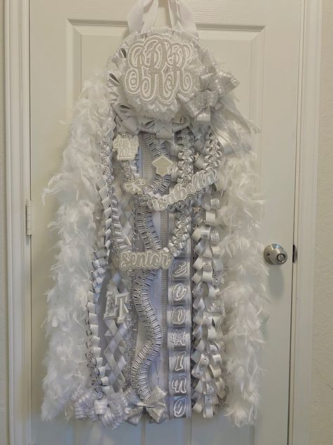 Senior white and silver heart shaped mega mum with white boa. Decorated with monogram and bear. morganmadegoods@gmail.com / morgan made on fb Senior really loved another mum and asked to make something very smiliar, they wanted to keep the same braids and structure. I used different ribbons and added perosnal touches. All White Senior Mum, White And Silver Senior Mum, All White Homecoming Mum, Silver And White Mums, White And Silver Homecoming Mum, Senior Year Mum, Hoco Mums Senior, Mum Ideas Homecoming Senior, Heart Shaped Homecoming Mums