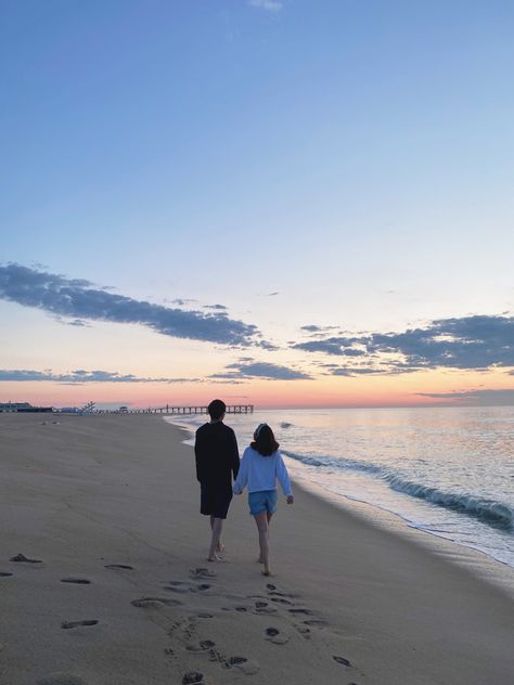 A couple is walking down the shore during sunrise. There are cotton candy skies + a boardwalk in the background Picture Sweet Couple, Beach Dating Aesthetic, Relationship Beach Aesthetic, Morning Date Aesthetic, Sweet Pictures Of Couples, Couple Things To Do Aesthetic, Beach Dates Couple, Sunrise Date Ideas, Beach Date Aesthetic Couple