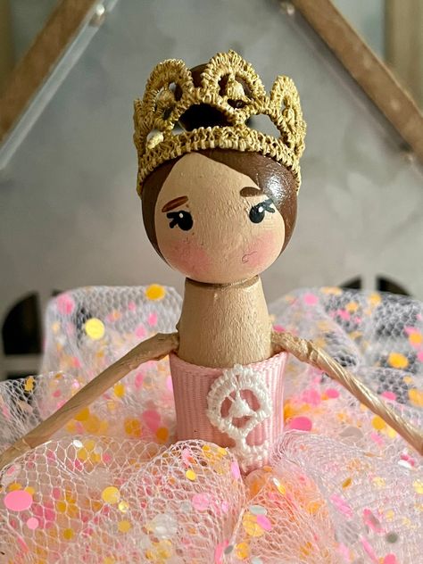 This sweet handmade Princess Ballerina clothespin figurine is dressed in a pink glittery polka dot tulle bubble dress with a pink satin top and wearing a gold crown on top of her head. She has brown hair in a bun on top of her head. She is made from a hand-painted wooden clothespin, a wooden bead head, and stands about 5 inches tall. This doll is a figurine but can be an ornament if wanted.  Things to keep in mind *This doll is for decorative purposes only and not intended as a toy. *Should not be handled by children under age 5 as small parts could come off and cause a choking hazard. *Product care: dust or wipe clean with a lightly damp cloth *Please keep in mind that each screen resolution is different so colors could vary slightly from image shown. Happy Shopping! Clothespin Ballerina Diy, Clothes Pin Ornaments, Diy Yarn Dolls, Pink Satin Top, Clothespin Doll, Princess Ballerina, Christmas Clothespins, Tutu Birthday, Doll Figurine