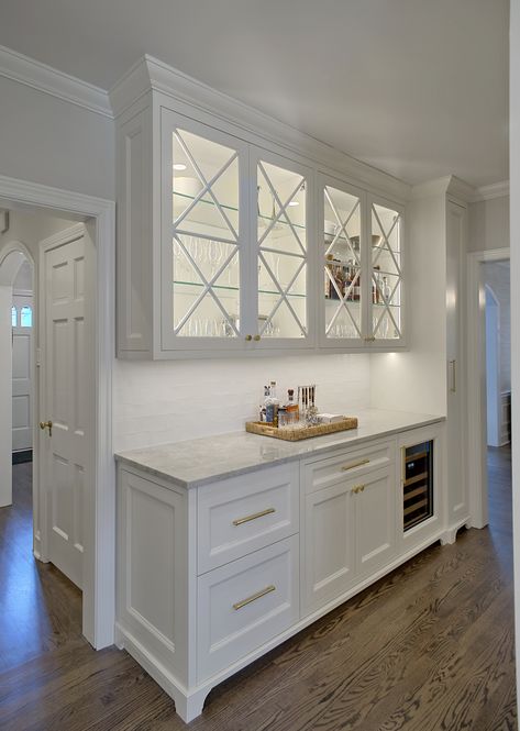 Custom home bar has temperature controlled wine storage and glass upper cabinets with lights for glassware display. Quartzite countertop, white ceramic backsplash and aged brass hardware add elegance to the space. Designed and constructed by Benvenuti and Stein. Norman Sizemore-photographer #benvenutiandstein #customcabinetry #homebar #drybar #eleganthomebar Kitchen With Some Glass Cabinets, Kitchen Cabinets With Frosted Glass Doors On Top, Kitchen Cupboard Glass Doors, Kitchen With Glass Upper Cabinets, White Kitchen Glass Cabinets Display Ideas, Bar With Upper Cabinets, Kitchen Cabinets Glass Uppers, White Kitchen Glass Cabinets, Kitchen Upper Cabinets Ideas