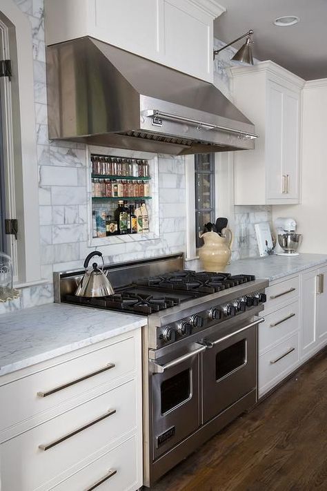 Lovely kitchen features a stainless steel kitchen hood fitted with a pot rack stands over a carrera marble subway tiled backsplash fitted with a tiled spice niche and a stainless steel stove flanked by arched windows illuminated by Boston Functional Library Wall Lights. Spice Niche, Stainless Steel Kitchen Hood, White Kitchen Set, White Kitchen Furniture, Viking Kitchen, White Kitchen Paint, Beautiful White Kitchens, White Kitchen Appliances, White Marble Kitchen