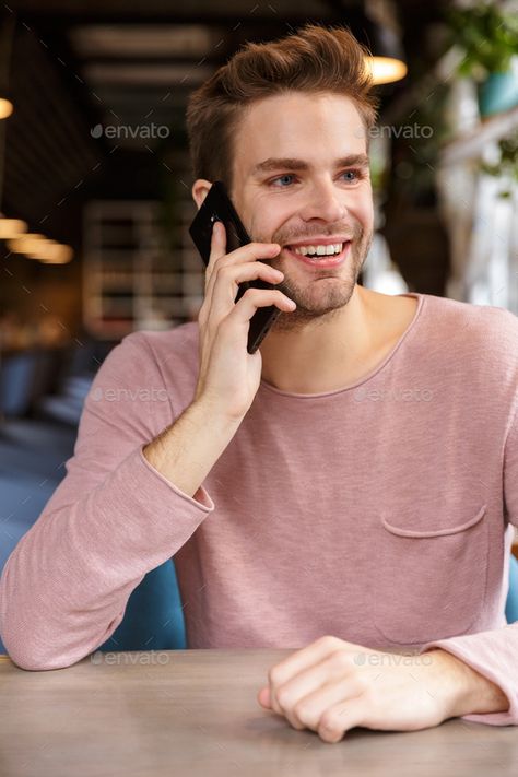 Attractive smiling young man talking on mobile phone by vadymvdrobot. Attractive smiling young man talking on mobile phone while sitting at the cafe table indoors #AD #man, #talking, #mobile, #Attractive Talking On Phone, Cafe Table, The Cafe, On Phone, Male Poses, Design Diy, Business Card, Card Design, Mobile Phone