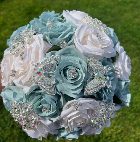 Handmade Quinceañera Bouquet/ Wedding.  With Light Sage Green and Ivory Roses. Finished off with Silver brooches and Butterflies.  *Please note brooches can change in style due to availability.* Decor / color combinations can be changed upon request. {This is a made to order Bouquet} Light Blue And Mint Green Wedding, Sage Green Teddy Bear Quince, Quince Ramos Sage Green, Wedding Bouquets With Butterflies, Sage Green And Silver Quinceanera Theme, Sage Green Ramos, Sage Green Quinceanera Bouquet, Sage Quince Nails, Sage Green Quinceanera Ramo