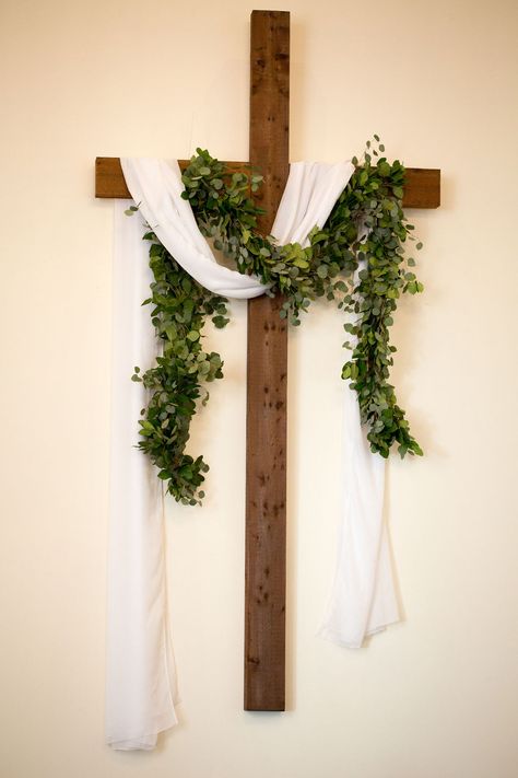 Wooden cross with white linen sash and thick greenery swag Easter Cross With Flowers, Wooden Cross Decor, Ordinary Time Church Decor, Church Easter Decorations Sanctuary, Easter Flower Arrangements For Church, Easter Church Decor, Cross Arrangements, Church Decorations Ideas, Ceremony Cross