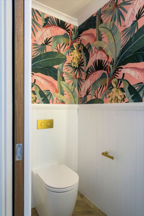 Fun Maximalism Powder Room | Maximalists and traditionalist unite in this little slice of the tropics. Herringbone laid wood-look tiles and VJ panelling speak of timeless style, while the pink and green banana palm wallpaper bursts with colour and unique expression. There’s so much to love in this separate toilet; in-wall cistern with plated buttons, brushed gold tap ware, cement Nood Co. hand basin and a stage stealing wall sconce. Toilet With Panelling And Wallpaper, Bathroom Ideas Quirky, Pink And Green Downstairs Toilet, Colourful Bathroom Wallpaper, Wallpaper Small Toilet, Colourful Small Toilet Room, Tropical Wallpaper Powder Room, Pink And Green Small Bathroom, Small Toilet With Wallpaper