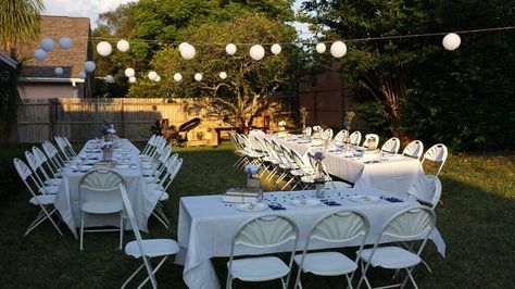 Navy blue graduation table setup outdoor backyard, white tablecloth, white chairs, white plates, gold ferrero rocher favors, wine bottle centerpieces with burlap, blue ribbon bow, twine, blue flower, baby's breath, rustic jar, white flower, white Chinese lanterns Ferrero Rocher Favors, White Chinese Lanterns, Blue Graduation Party, Blue Ribbon Bow, Graduation Table, Wine Bottle Centerpieces, Gold Graduation Party, Graduation Tables, Bottle Centerpieces