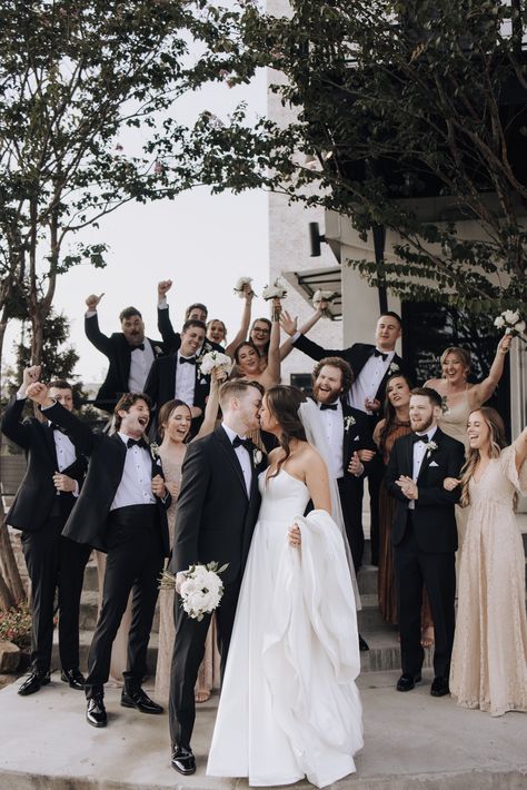 Celebrating love with the best bridal party! The bridal party's outfits match the champagne and black theme, while the bride and groom steal the spotlight with a sweet kiss. | Photo: Mandi Roach Photography 

Spotlight WiH Partners- 
Venue: The Astorian
Wedding Entertainment: Intensity Bands Houston 

#WeddingsinHouston #BridalParty #WeddingPhotography #BridesmaidsDresses #HoustonWedding #HoustonVenue #BridalInspo Tan And Black Bridal Party, Bridal Party Photos Champagne, Blurry Bridal Party Photo, City Bridal Party Photos, Documentary Style Bridal Party Photos, Chic Wedding Venues, Bridal Party Photography, Hill Country Wedding Venues, Industrial Chic Wedding