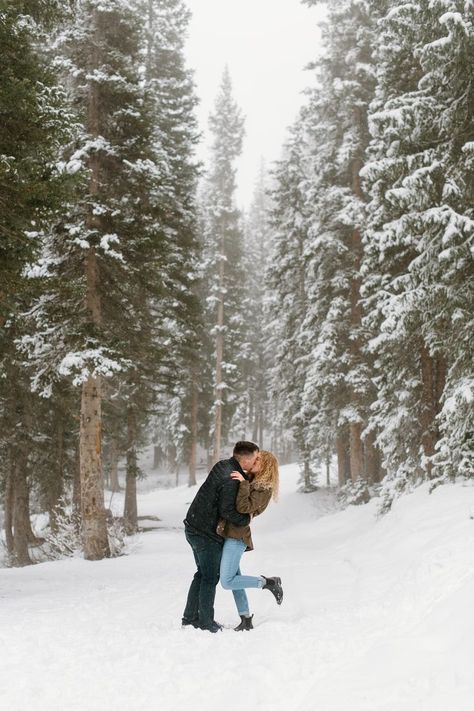 couple is sharing a kiss in the middle of a snow covered pine forest, woman is popping her foot Winter Engagement Photos Snow, Winter Couple Pictures, Couple Photography Winter, Snow Engagement Photos, Utah Winter, Winter Engagement Pictures, Snow Photoshoot, Engagement Picture Outfits, Cute Engagement Photos