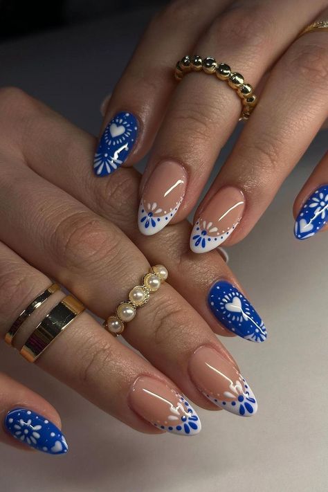 These almond-shaped nails are a playful mix of summer vibes with a contrasting design. The vibrant blue base pops with white floral patterns and heart shapes, while the clear nails are elegantly simple with a hint of white floral art and subtle line accents. The pairing of bold and subdued creates a lovely and engaging aesthetic perfect for sunny days.  // Photo Credit: Instagram @chibimoon.nails Oval Shaped Summer Nails, Nails Almond Short Design, White And Blue Nails With Designs, Summer Subtle Nails, Short Almond Nails Designs Summer 2024, Nail Art Vacation, Nails Acrylic Summer Blue, Summer Greece Nails, Blue Nails With White Design