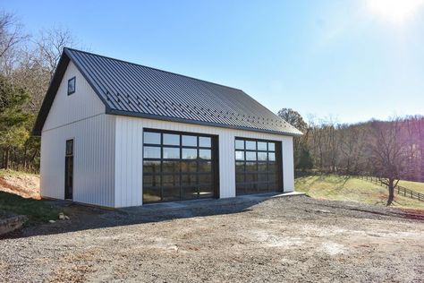 This is a 30x40x12 garage that we recently completed. It features glass garage doors from Clopay's Avante series, creating a modern, firehouse aesthetic. Check out our website for more garage ideas! White Garage With Black Doors, Metal Building With Glass Garage Doors, Garage Ideas Exterior, Garage With Glass Doors, White And Black Garage, Separate Garage From House Modern, Detached Metal Garage Ideas, Modern Detached Garage, Black Modern Garage Door