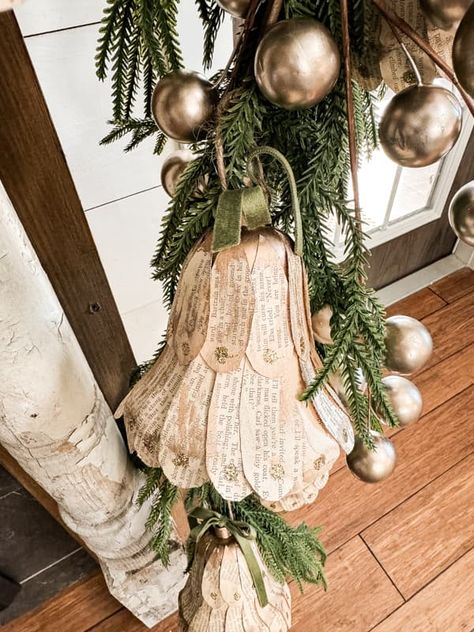 DIY Christmas Bells with old book pages on mantel greenery garland. Diy Christmas Bells Decorations, Dollar Tree Bells, Mantel Greenery, Diy Christmas Bells, Christmas Paper Chains, Book Page Garland, Vintage Inspired Christmas, Antique Christmas Ornaments, Handcrafted Ornaments