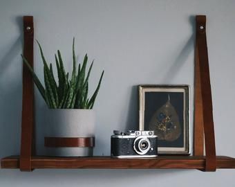 Leather strap shelves are a simple, easy and cheap way to change your interior. They will add a unique character and make the shelves a unique decorative element in your home. You can do it yourself! Leather Strap Shelf, Nursery Shelving, Leather Shelf, Leather Strap Shelves, Shelves Plant, Leather Home Decor, Pallet Wall Shelves, Shelving Brackets, Leather Kitchen