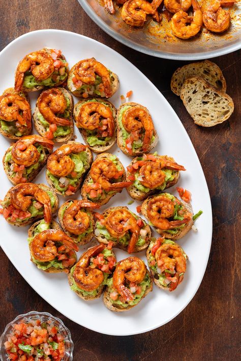 These Shrimp Crostini bites are an easy crowd pleasing appetizer that comes together in less than 30 minutes. Toasted baguette is topped with guacamole, fresh salsa, and spicy cajun shrimp. These make delicious party finger food or a fun and fancy movie night snack all year round! Bday Dinner Party Ideas, Shrimp Finger Food Party Appetizers, Easy Bday Party Food, Bday Party Snacks Finger Foods, Fancy Party Snacks, Dinner Party Finger Food Ideas, Shrimp Finger Food, Shrimp Crostini Appetizers, Appetizer Recipes Wedding