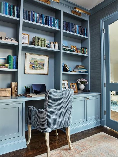 A blue desk chair sits at a blue built-in desk fixed beneath blue built-in bookshelves lit by antique brass picture lights. Blue Built Ins, Garage Remodel Ideas, Remodel Garage, Built In Desk And Shelves, Studio In Casa, Blue Bookshelves, Den Library, Built In Bookshelves, Bookshelf Lighting