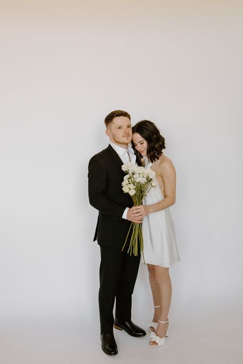 Engaged couple in black suit and white silk dress with florals posed in studio with flower bouquet Engagement Photo Studio, Studio Engagement Shoot, Studio Engagement Photos, Photos With Flowers, Engagement Shoots Poses, Portraits Poses, Wedding Photo Studio, Natural Light Studio, Anniversary Pictures