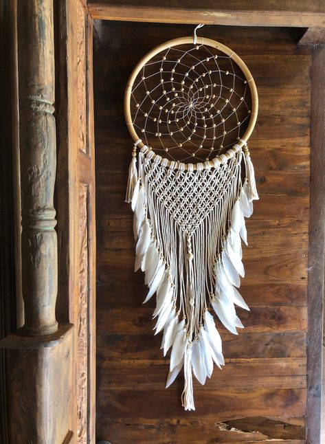 This beautiful large handmade white crochet and macrame dream catcher is a perfect boho wall hanging for home decor. Made with love and good vibes it's perfect for a bohemian bedroom, nursery room, kids bedroom, or living room. Dream catchers originate from Native American cultures. The dream catcher is believed to protect a person from bad dreams.  The good dreams filter down through the feathers and gently reach the dreamer while the bad dreams get caught. Dream catchers are believed to bless someone with pleasant dreams, good luck, and harmony. They are perfect gifts for loved ones as they carry good meaning and intention.  Right now we could all use that! This dream catcher is made in the local village of Tegalalang close to where we are staying until we are able to return home. We wil Beaded Dream Catcher, Handmade Wall Hangings, Dreamcatcher Design, Dream Catcher White, Healing Room, Macrame Dream Catcher, Small Dream Catcher, Macrame Boho, Dream Catcher Boho