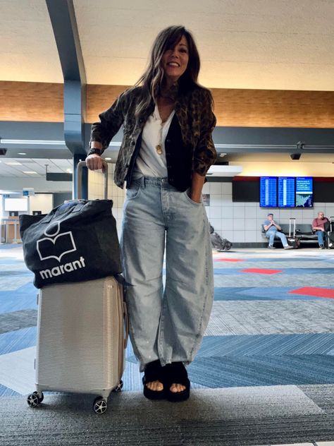 Woman posing at the airport dressed in barrel leg jeans, white shirt, black vest, and black sandals. Puddle Jeans Street Style, Barrel Denim Outfit, Baloon Jeans Styling Women, Barrel Jeans Outfit Spring, Diy Barrel Jeans, Free People Barrel Jeans, Barrel Jeans Outfit Street Style, Styling Barrel Jeans, Ballon Jeans Outfits