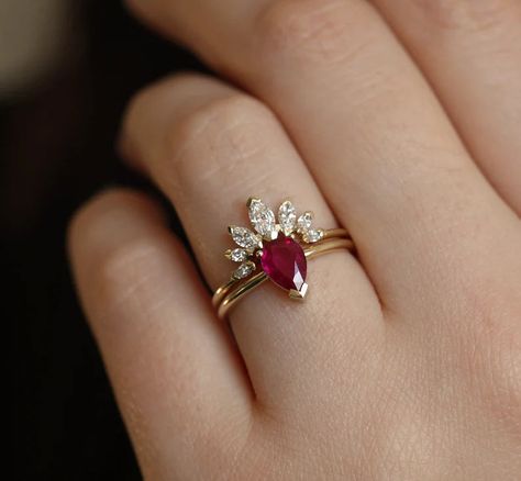 A stunning ring set consisting of a solitaire ruby engagement ring and a marquise moissanite band. This is adjustable and can be personalized. Details:Main gemstone: Genuine RubyShape: Pear Measurements: 0.75 - 0.80 carat (Approximately)Band measurements: 1.6mm (Approximately)Material: 18k Yellow Gold, White Gold, Rose Gold, Platinum (additional fee)Sizes available: 3-8 (Larger and smaller sizes are available as well. Priced upon request.) Ruby Engagement Ring Set, Diamond Crown Ring, Ruby Wedding Rings, Diamond Crown, Gold Ring Designs, Ruby Engagement Ring, Crown Ring, Rose Gold Engagement, Engagement Ring Set