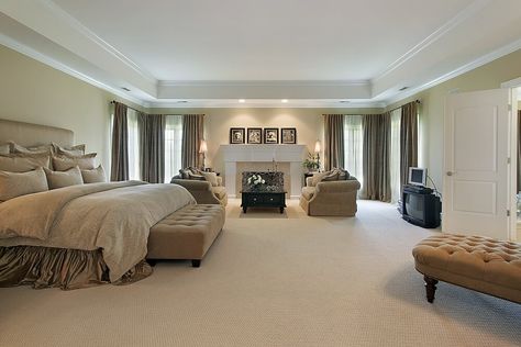 This spacious, carpeted master bedroom has an enormous tray ceiling with vents and recessed lighting around it. The fireplace on the far wall has its own seating area with two cozy sofas and a black coffee table. Large Bedroom Furniture, Rectangular Bedroom, Long Bedroom, Wide Bedroom, Big Bedroom, Bedroom Remodeling, Huge Bedrooms, Private Bedroom, Chic Dresser