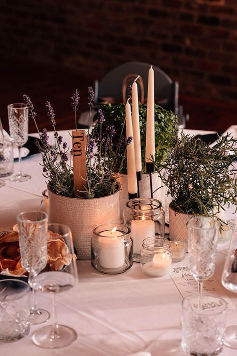 Potted plants of rosemary and lavender with a wooden table number sign along with white taper candles in black candleholder with smaller tea lights and pillar candles Tea Light Table Decorations, White Taper Candles, Taper Candles Wedding, Tea Lights Wedding, Wedding Playlist Reception, Pillar Candles Wedding, Table Number Sign, Wedding Candles Table, Candle Table Decorations